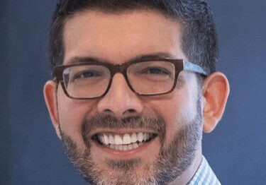 A man with glasses smiling warmly at the camera.