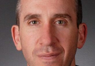 Close-up portrait of a middle-aged man with short hair and a neutral expression.