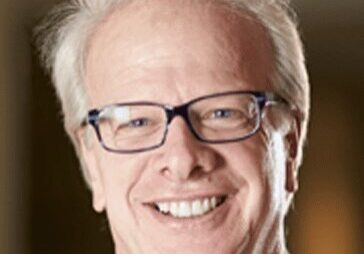 Smiling older man with glasses and white hair.