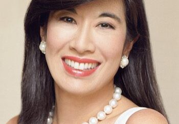 A smiling woman with long dark hair wearing pearl earrings and necklace.