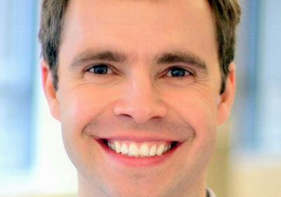 Smiling man with light brown hair in a close-up portrait.