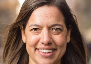 Smiling woman with long brown hair outdoors.