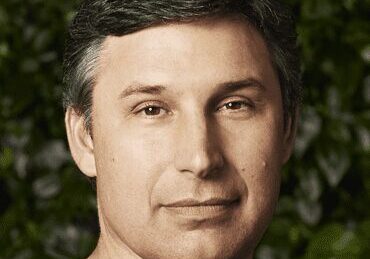 Portrait of a middle-aged man with dark hair against a leafy background.