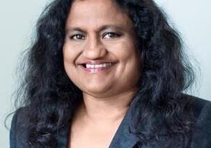Smiling woman with dark curly hair in a blazer.