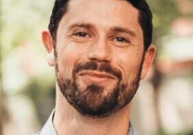 Portrait of a smiling man with a beard in an outdoor setting.