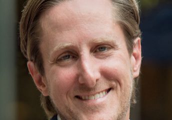Smiling man with light hair in a blue suit jacket.