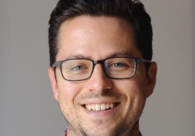 Smiling man wearing glasses and a checkered shirt.