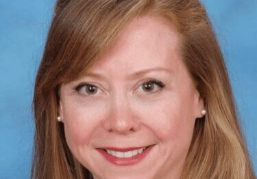 Portrait of a smiling woman with light brown hair against a blue background.