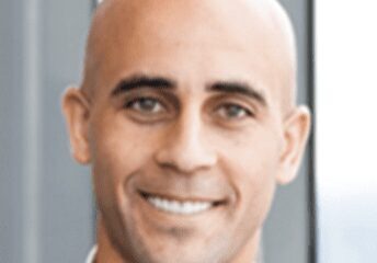 Smiling bald man in a suit with a blurred background.