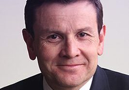 Portrait of a man in a suit and tie with a neutral background.
