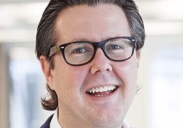 Smiling man with glasses and dark hair in a professional setting.