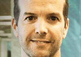 Portrait of a smiling man with short hair and light facial stubble.