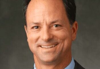 Professional headshot of a smiling middle-aged man in a suit.