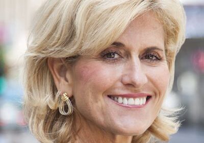 Smiling mature woman with short blonde hair and elegant earrings.