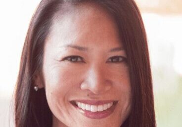 Smiling woman with long dark hair in a softly lit setting.