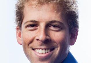 Smiling young man with curly blonde hair wearing a blue shirt.