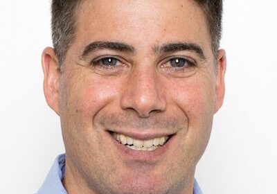 Portrait of a smiling man with short dark hair and a light blue shirt.