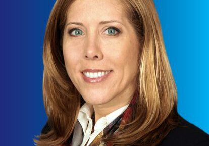 Professional woman with light brown hair wearing business attire against a blue background.