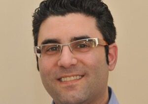 A smiling man with glasses and curly hair.