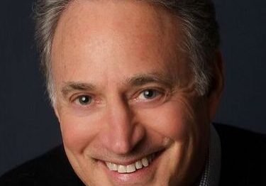 Smiling middle-aged man with gray hair against a dark background.