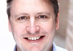Smiling middle-aged man in a collared shirt with a blurred background.