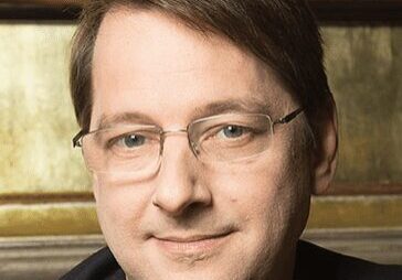 Portrait of a man wearing glasses and a suit, smiling gently.