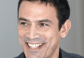 Smiling man with short dark hair in a gray suit jacket.