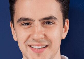 Portrait of a young man smiling against a dark blue background.