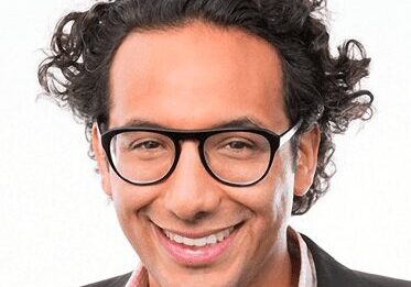 Smiling man with glasses and curly hair in a casual blazer.