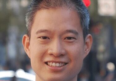 Portrait of a smiling man outdoors with blurred background.