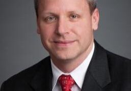 Professional man in a suit and red tie poses against a grey background.