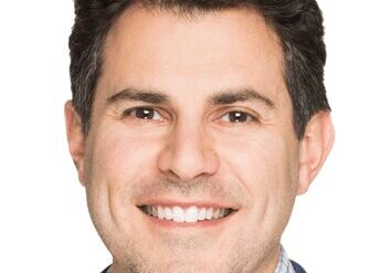 Headshot of a smiling man with dark hair in business attire.