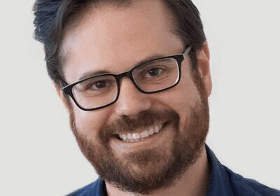Smiling man with glasses and beard in a blue shirt.