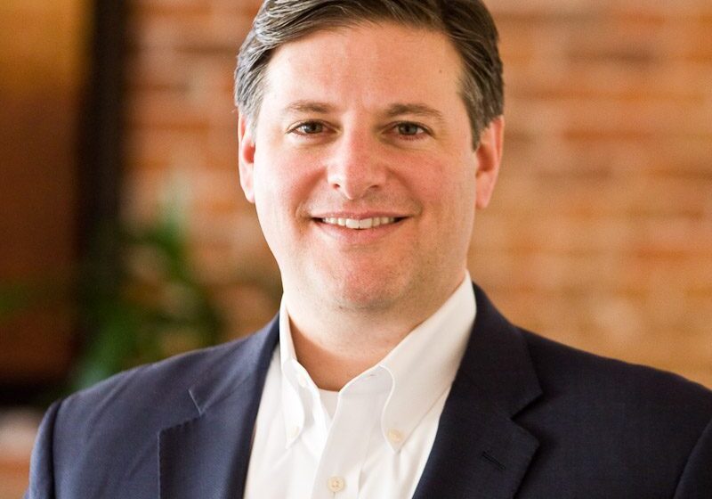 Professional man in a suit smiling against a brick wall.