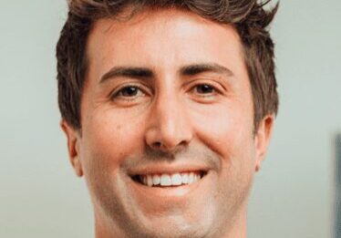 A smiling man with tousled brown hair in a casual setting.