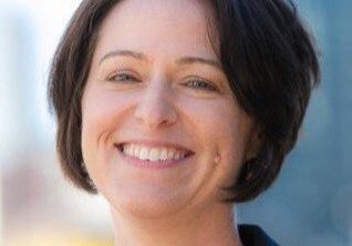 Smiling woman with short dark hair outdoors.