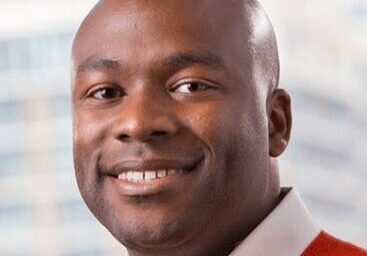 Portrait of a smiling man wearing a red sweater with a blurred background.