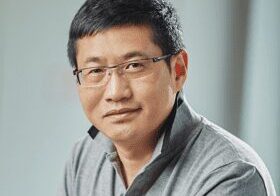 Portrait of a middle-aged man wearing glasses and a gray shirt.