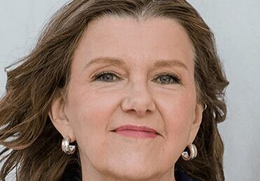 A confident middle-aged woman with styled hair and pearl earrings.