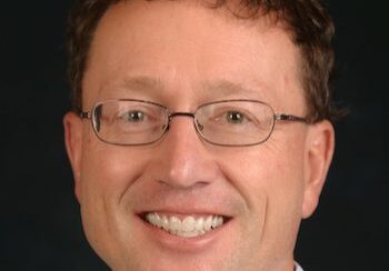 Smiling man with glasses and curly hair.