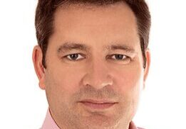 Portrait of a man with short dark hair wearing a light pink shirt.