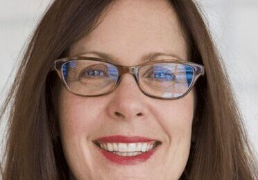 Smiling woman with glasses and long brown hair.