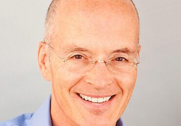 Smiling bald man wearing glasses and a light blue shirt.