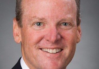 Professional headshot of a smiling man in a suit and tie.