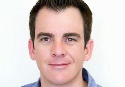 Portrait of a smiling man with dark hair against a white background.