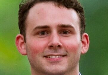Portrait of a smiling young man with short brown hair outdoors.