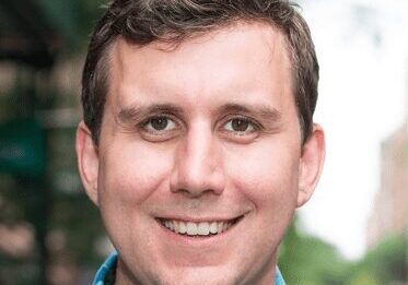 Smiling man with short brown hair in a casual setting.