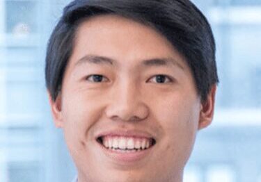 Smiling young man with short black hair in a light blue shirt.