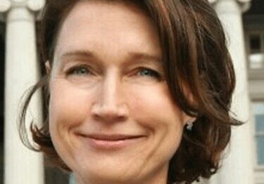 Woman with short brown hair smiling outdoors in front of columns.