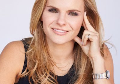 Smiling blonde woman with long hair wearing a black sleeveless top.